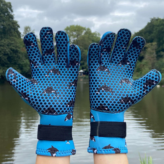 Blue neoprene gloves with black patterns on a background of water and trees