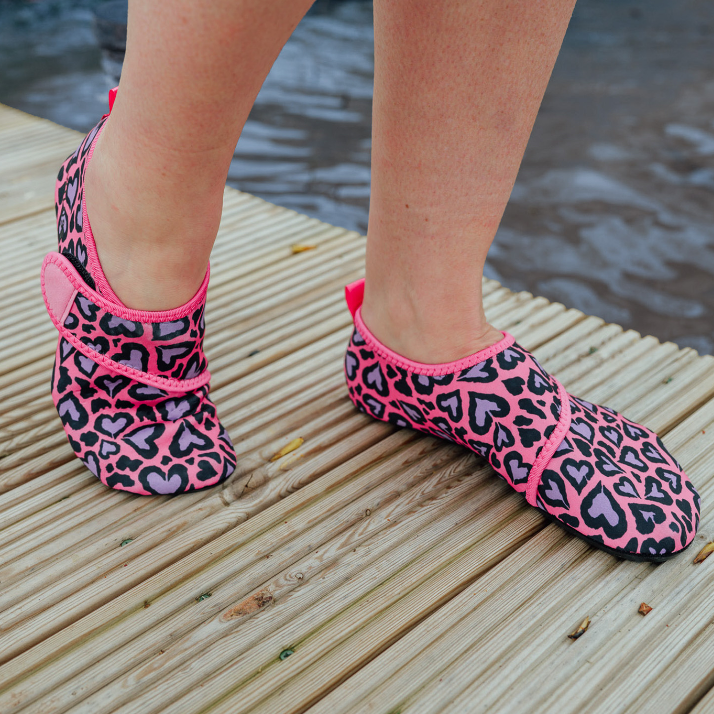 Pink and black patterned neoprene beach shoes on a wooden dock with water in the background