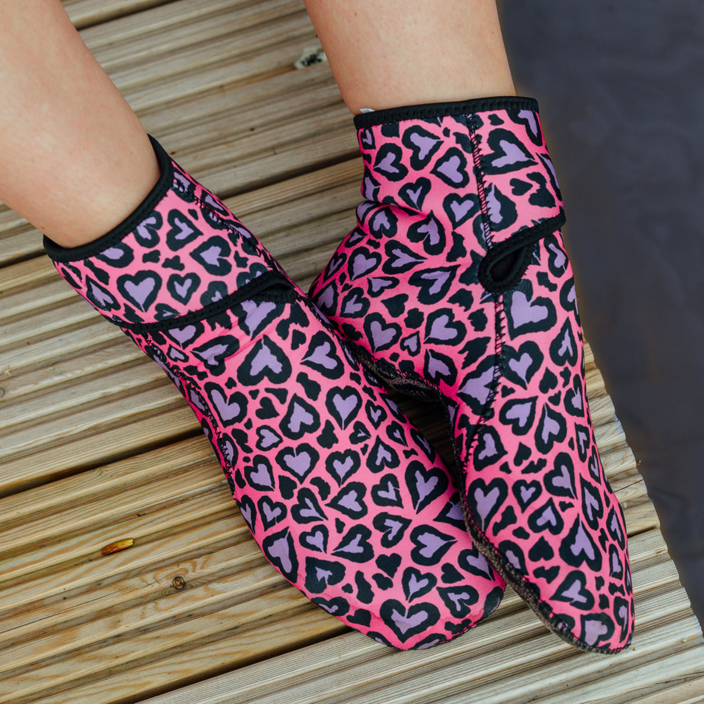 Pink and purple heart-patterned neoprene socks on a wooden surface