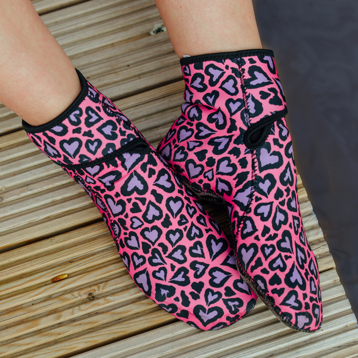 Pink and purple heart-patterned neoprene socks on a wooden surface