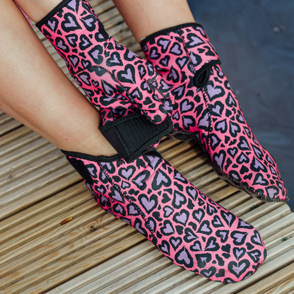 Pink and black heart-patterned neoprene socks on a wooden floor.