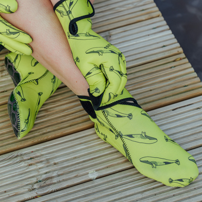 Yellow neoprene gloves with velcro strap and whale pattern on a wooden surface