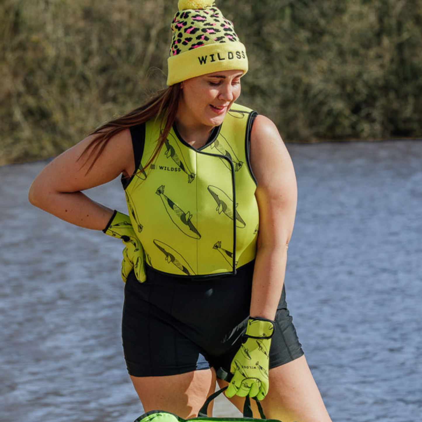 Person wearing a yellow and black outfit with whale print pattern stood lakeside outdoors.