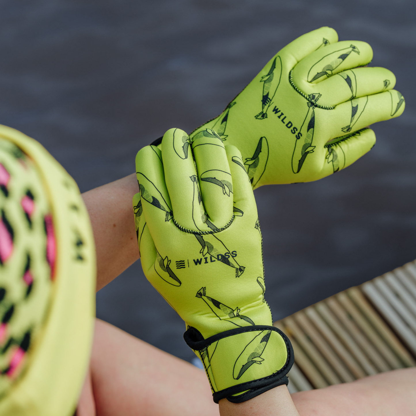 Bright yellow neoprene gloves with black whale patterns held by a person against a blurred natural background