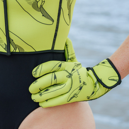 Person wearing bright yellow neoprene gloves with black whale patterns, sitting by a body of water.