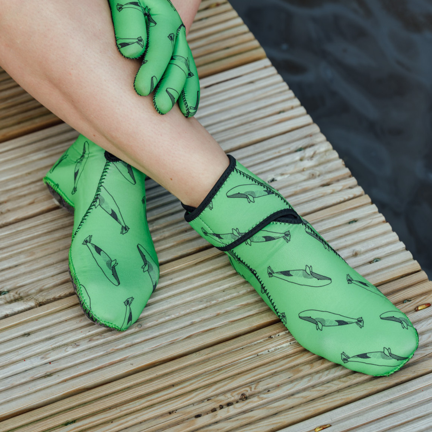 Green neoprene gloves with whale pattern on a wooden surface