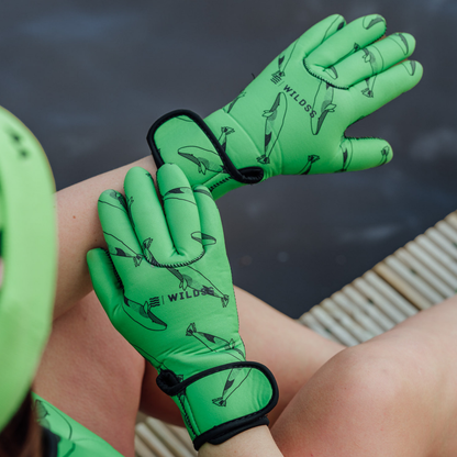 Green neoprene gloves with whale designs on a person's hands against a blurred natural background