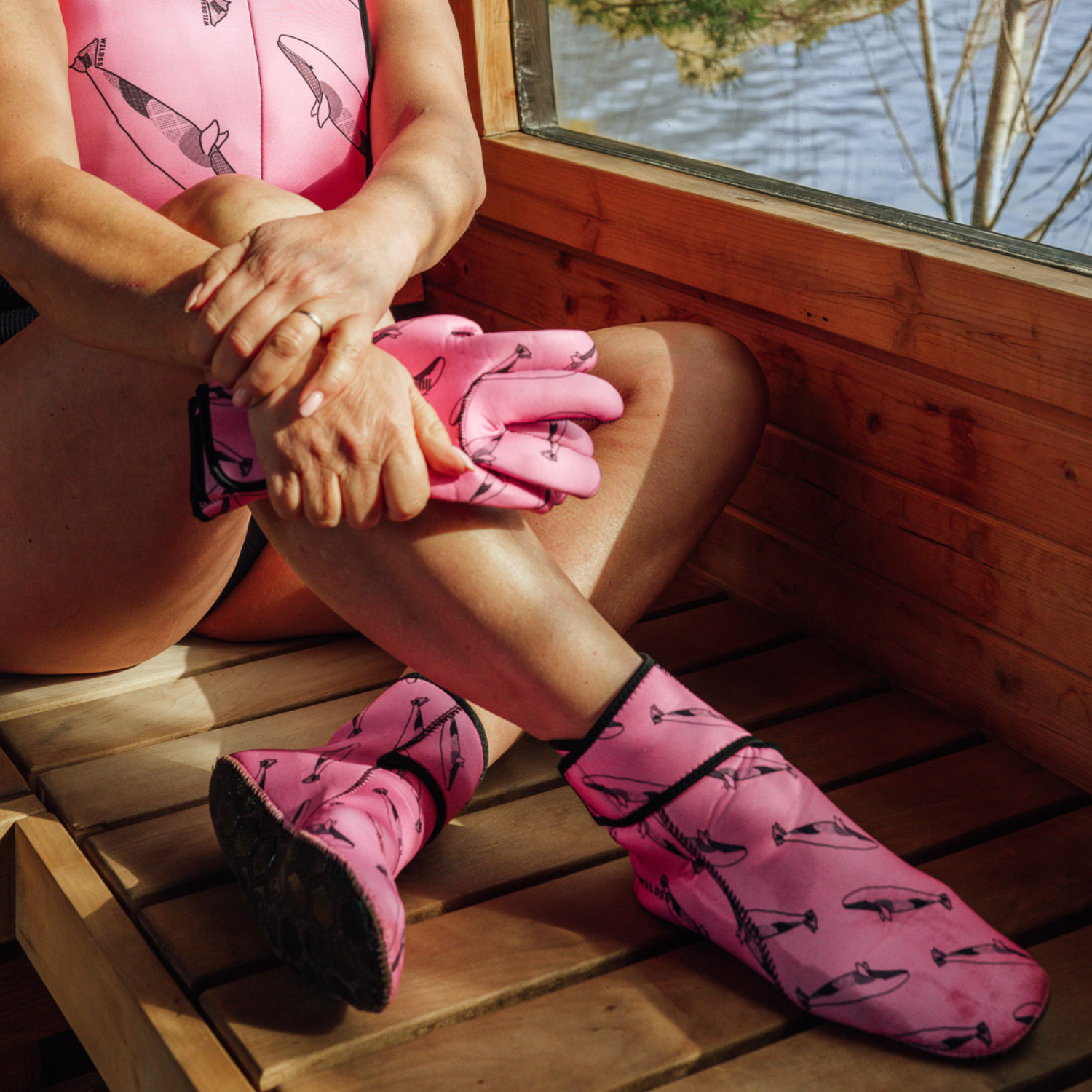 Person wearing pink neoprene gloves, body warmer and socks with whale design sitting in a wooden sauna