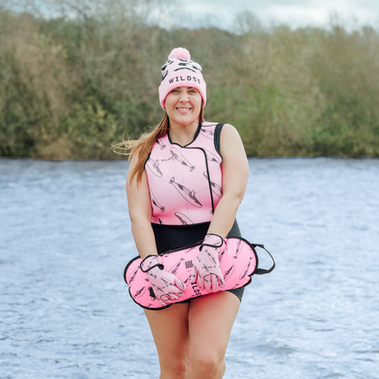 Woman wearing a pink neoprene body warmer  and beanie by a body of water